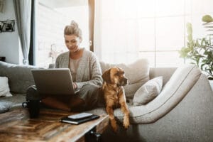 a woman works on the couch with her dog