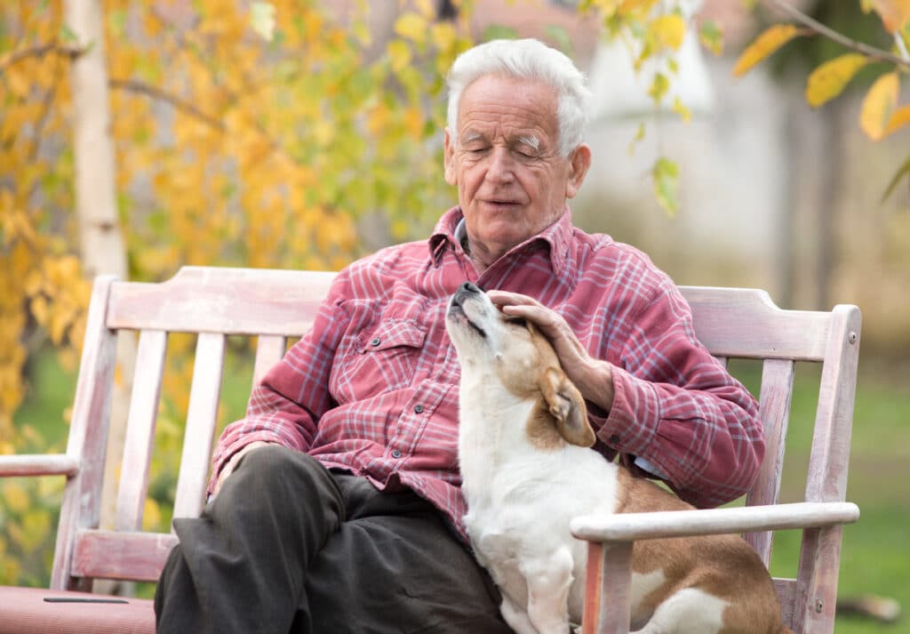 An older man sits on a bench with his dog.
